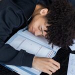 tired mixed race man lying on an opened book and homework papers