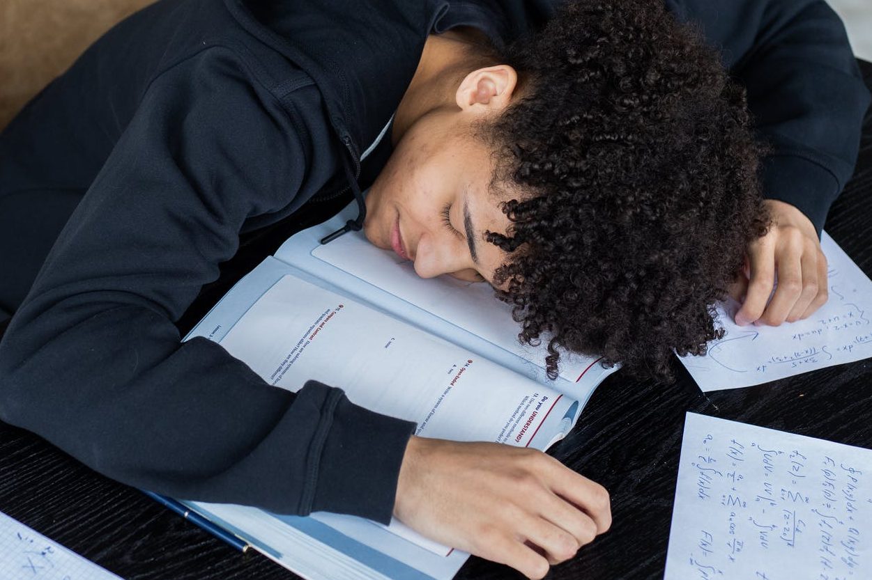 Man lying asleep on opened textbook and homework papers
