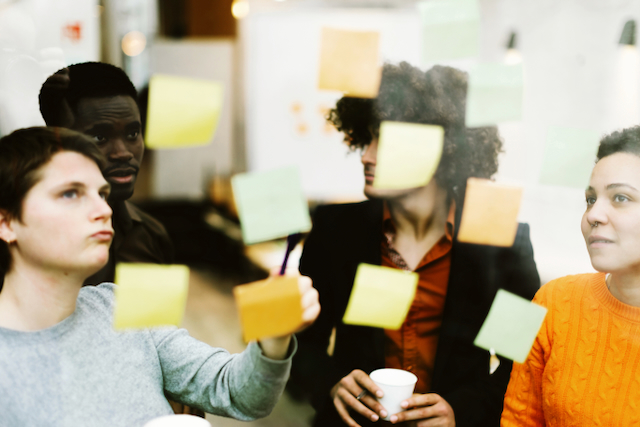 team of young creatives discussing and brainstorming in front of colourful notes attached to glass