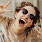Laughing woman in dark glasses showing victory sign in both hands.