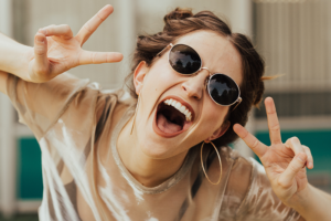 Laughing woman in dark glasses showing victory sign in both hands.