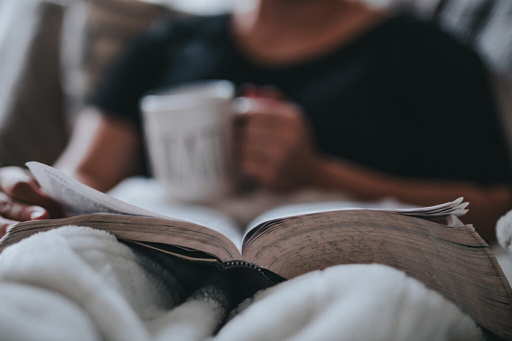 Soft focus person holding a coffee mug reading a book open on her lap.